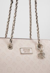 Ljusrosa läderhandväska med präglade mönster, silverdetaljer och kedjeremmar med detaljer, inklusive en märkesberlock.