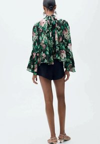 Blommig blus i mörkgrön, med luftiga ärmar och knytning vid halsen, kombinerat med svarta shorts. Lättvikts, halvgenomskinligt material.