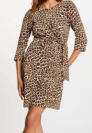 Frau trägt ein knielanges Kleid mit Leopardenmuster, dreiviertellangen Ärmeln und einer seitlichen Bindung an der Taille.