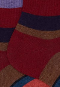 Nahaufnahme von bunten gestreiften Stricksocken in Rot, Marineblau, Braun, Lila, Blau und Orange, die übereinanderliegen.