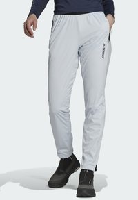 Pantalones exteriores de color gris claro con cintura elástica, bolsillos con cremallera y detalles en negro. Confeccionados con un material suave, ligero y transpirable.