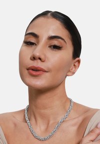 Collier en chaîne en argent avec des maillons entrelacés, présentant une finition texturée. Porté autour du cou sur un fond neutre.