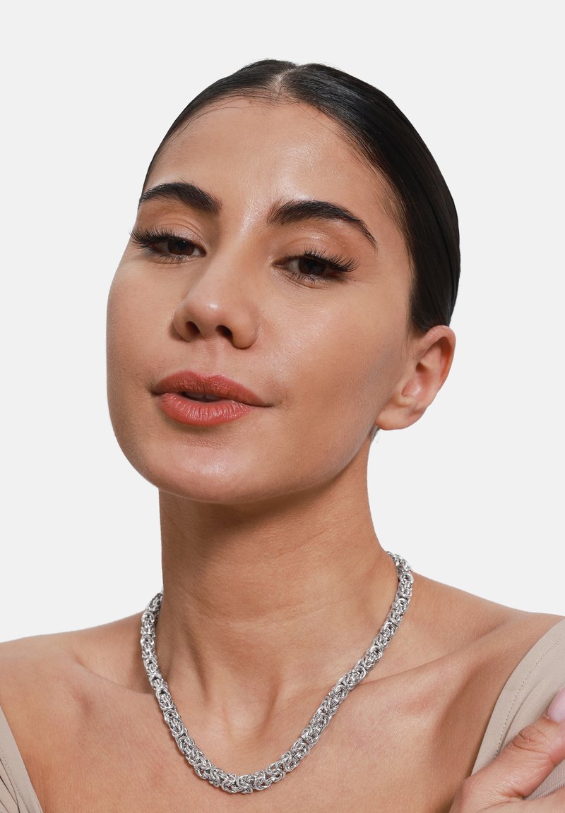 Collier en chaîne en argent avec des maillons entrelacés, présentant une finition texturée. Porté autour du cou sur un fond neutre.
