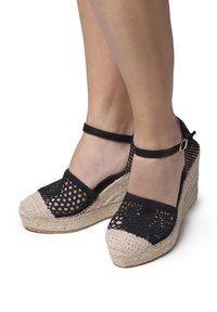 Sandales compensées en espadrille tissées noires avec une semelle en jute naturel, présentant une bride à la cheville noire et un design à bout ouvert.
