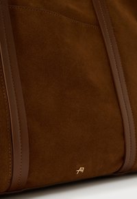 Pruun seemisnahast käekott, millel on siledast nahast detailid ja sangad. Omab minimalistlikku kuldset logo, rõhutades puhast ja elegantset disaini.