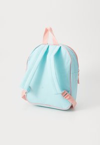 Mochila pequena, azul clara e rosa, de pé, com alças almofadadas e pega rosa, em fundo branco.