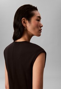 Svart ermeløs kjole med høy hals og skjult glidelås bak, komplettert med en glatt tekstur og strukturert passform.