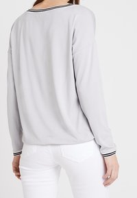 Helles graues Langarmoberteil mit schwarz-weißer gestreifter Halslinie, lässiger Schnitt und weicher Textur, kombiniert mit weißen, enganliegenden Hosen.