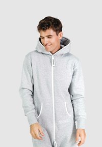 Grijze zip-up onesie gemaakt van zachte katoen. Heeft een capuchon, twee voorzakken met witte rand en een geborduurd logo op de borst.