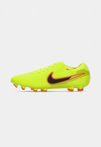 Botín de fútbol amarillo brillante con una superficie texturizada, el famoso swoosh negro de Nike y detalles en naranja. Presenta un diseño con cordones y tacos moldeados.