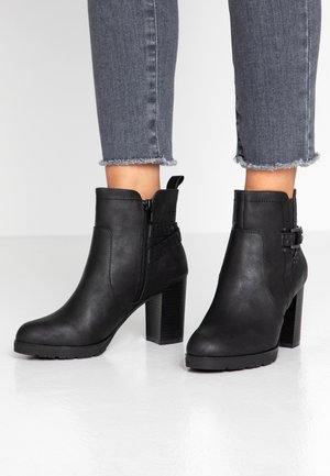 Botas negras hasta el tobillo con un acabado suave, cremallera lateral, correa decorativa y una suela de tacón grueso. Tienen una punta redondeada y acentos texturizados.