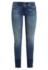 Jeans ajustados en denim azul medio, con un lavado desgastado, diseño estándar de cinco bolsillos y dobladillo deshilachado en el tobillo.