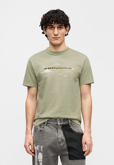 Πράσινο ελιάς βαμβακερό t-shirt με λαιμόκοψη κανονική, που φέρει ξεθωριασμένο γραφικό τύπωμα σε χρυσό και γκρι στο στήθος.