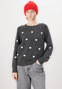 Gray knit sweater with white heart patterns, rounded neckline, and long sleeves, paired with light gray pants and a bright red knit beanie.