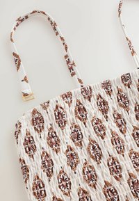 Geantă din material alb, cu textură pliată, având un model floral în nuanțe de maro și roșu. Include două bretele subțiri și un detaliu din metal de culoare aurie.