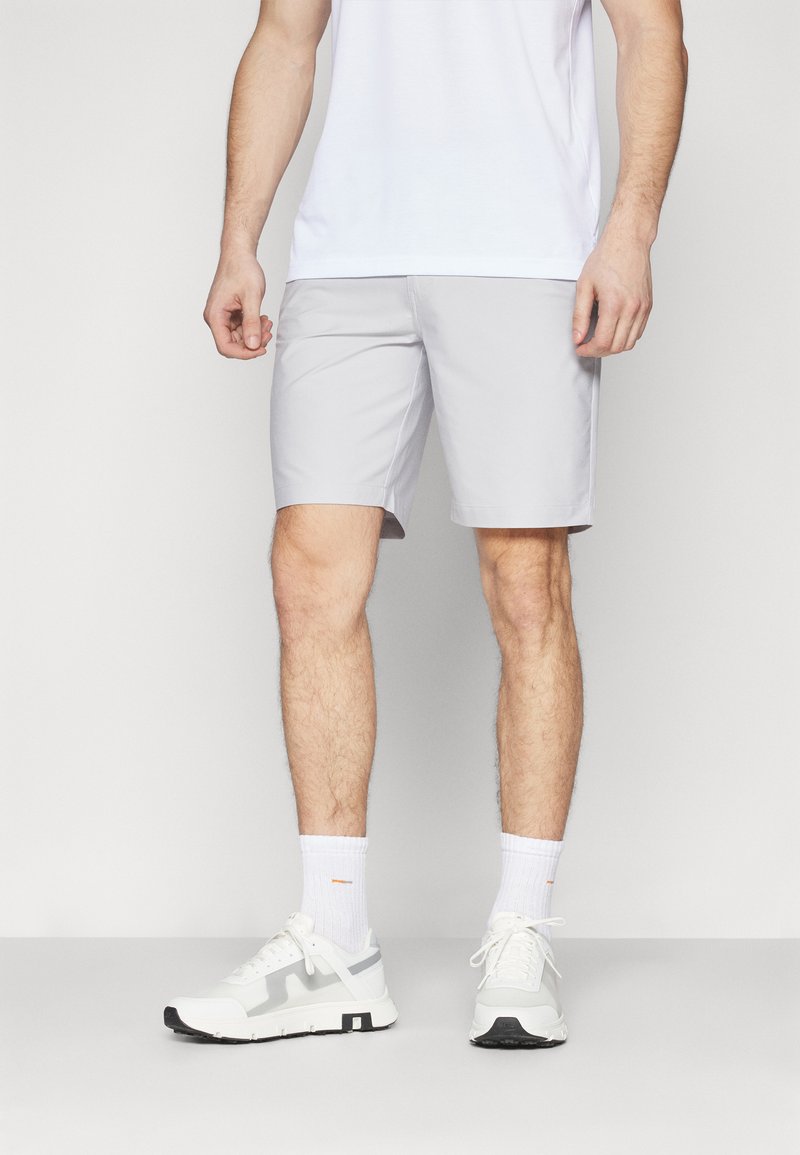Lys grå shorts med en glatt tekstur, knelengde, kombinert med hvite joggesko og trening sokker. Enkel, funksjonell design.