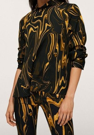 Czarna bluzka z długim rękawem i spodnie z wirującym wzorem marmuru w kolorach złotym i brązowym, prezentowane na osobie z podwiniętymi rękawami.