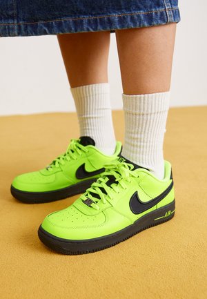 Baskets Nike vert néon avec des accents noirs, en cuir texturé, à bout rond, avec des lacets plats et une semelle en caoutchouc ; portées avec des chaussettes blanches à côtes.
