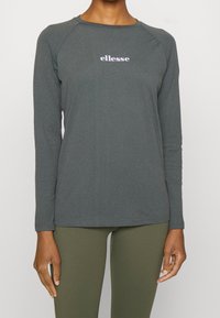 Czarna koszula z długim rękawem z ciemnoszarej bawełny z okrągłym dekoltem. Posiada fioletowe logo "ellesse" na klatce piersiowej oraz rękawy raglanowe.