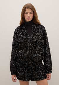 Black sequin jacket with a zip front, long sleeves, and a relaxed fit, paired with matching shorts. Smooth texture, reflective accents.