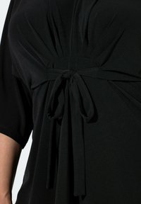 Černý top z měkkého materiálu s nařaseným, skládáním ve středu pasu, které zvýrazňuje detail se zavázáním pro úzký siluetu.