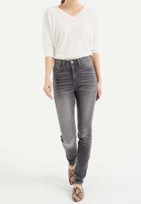 Light grey high-waisted jeans with faded detail, paired with a white V-neck top and snake-print slip-on shoes. Smooth fabric and fitted design.
