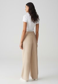 Beige brede broek met een hoge taille en een zachte textuur. Gecombineerd met een fitting wit T-shirt met korte mouwen, dat een minimalistisch ontwerp toont.