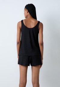 Top in cotone nero senza maniche con scollatura sul retro, abbinato a pantaloni corti neri coordinati. Il tessuto sembra morbido con una vestibilità rilassata.