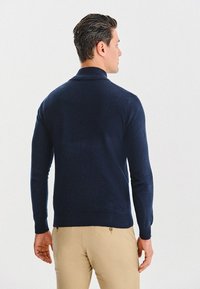 Granatowy sweter z dzianiny z kołnierzykiem, ściągaczami na mankietach i u dołu. Tkanina wydaje się miękka i teksturowana, zaprojektowana z myślą o luźnym kroju.