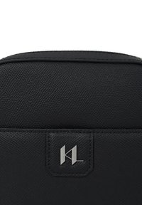Geantă din piele neagră texturată, cu o placă metalică argintie cu logo-ul KL cusută pe panoul frontal.