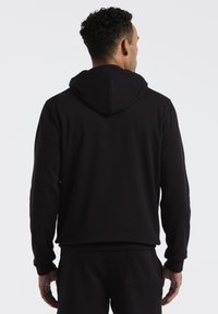 Zwarte hoodie met een kangoeroezak, ribgebreide manchetten en een capuchon met trekkoord, gemaakt van zachte, gestructureerde stof. Achteraanzicht weergegeven.