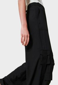 Pantaloni cargo neri con una vestibilità rilassata, dotati di più tasche, una texture liscia e un alto punto vita. Accenti di cuciture visibili.