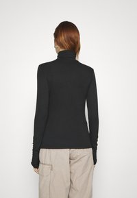 Svart ribbestrikket turtleneck med lange ermer, tettsittende design, myk tekstur, sammen med løse, lyse beige cargo-bukser med sidelommer.