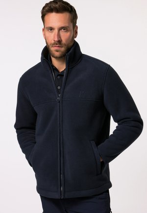 Navy fleece jacket with high collar and zipper, featuring two side pockets and a subtle logo on the chest. Soft texture and casual design.