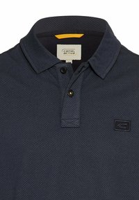 Marineblauwe poloshirt met een textuurpatroon, drieknopsluiting, vlakke kraag en een logo-opdruk op de borst. Materiaal lijkt ademend.