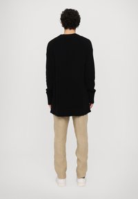 Black ribbed sweater, long sleeves, oversized fit, paired with beige linen trousers and white sneakers, viewed from the back.