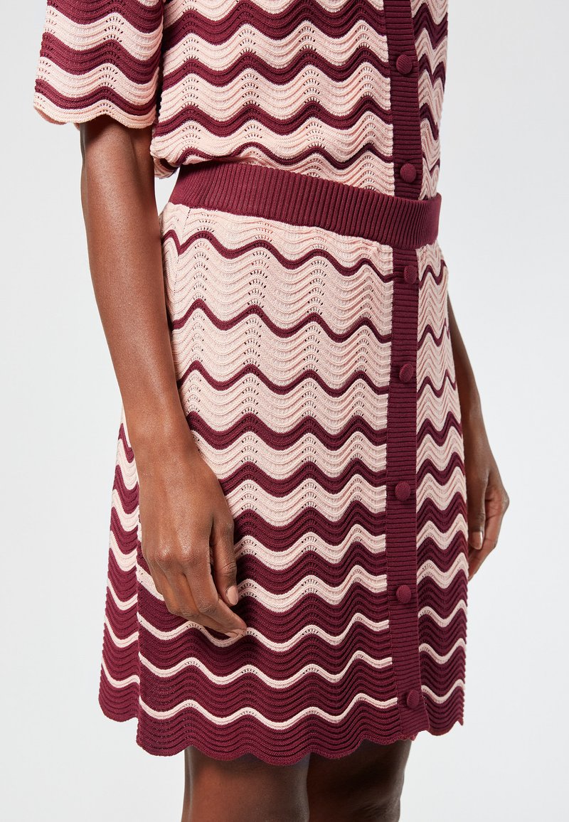 Neulemekko, jossa on vuorottelevia aaltoilevia raitoja burgundissa ja pehmeässä vaaleanpunaisessa, napitus edessä, ribattu vyötärö ja aaltoileva helma.