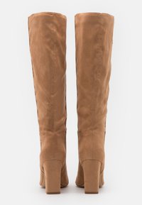 Botas de ante de color beige hasta la rodilla con una textura suave, tacones cuadrados y un diseño minimalista. Sin herrajes ni patrones visibles.