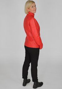 Röd läderjacka med ståkrage, figursydd design och långa ärmar, kombinerad med svarta byxor och ankelboots.