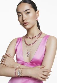 Schmuckpräsentation: pinkes Satin-Kleid, geschichtete Halsketten mit verschiedenen rosa Steinen, Perlenanhänger, passende Ohrringe und mehrere Armbänder aus unterschiedlichen Metallen.