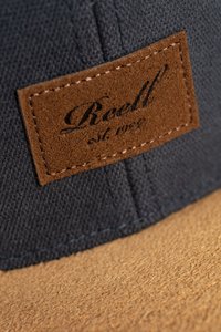 Dunkelblaues Cap aus strukturiertem Stoff mit einem beigefarbenen Wildlederpatch, das eingravierten Text zeigt. Der Schirm ist leicht braun und hat eine flache Form.