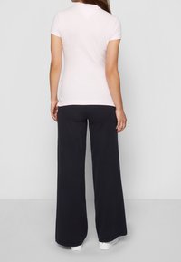 Jasnoróżowa koszulka z krótkim rękawem w połączeniu z luźnymi, ciemnogranatowymi spodniami o gładkiej fakturze i prostym wzorze.