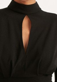 Černé šaty s vysokým límcem a výstřihem ve tvaru klíčové dírky na krku. Tkanina je hladká s strukturovanou siluetou.