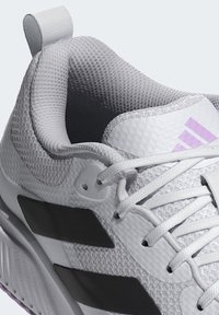 White athletic shoe with mesh upper, black accents, textured fabric, and purple logo. Features a padded collar and flat laces.