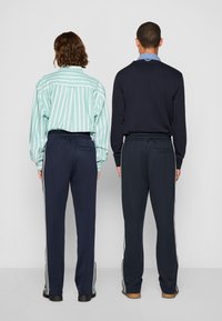 Des tenues décontractées comprenant une chemise rayée verte et un haut à manches longues bleu marine, associés à un pantalon bleu marine avec des rayures blanches sur les côtés et des ceintures élastiques.