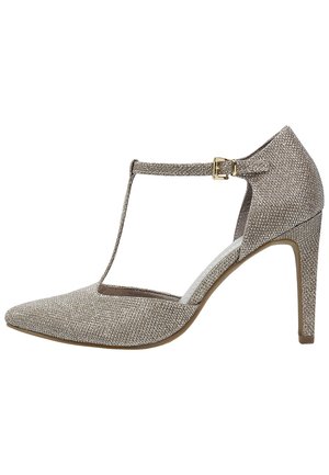 Czółenka na wysokim obcasie z ostrym noskiem, wykonane z metalicznego materiału w jasnym beżu, z paskiem T i akcentem w postaci klamry na kostce.