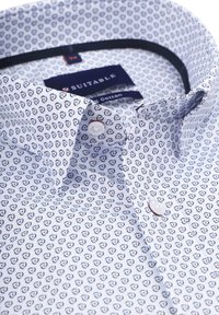 Wit katoenen overhemd met een draaierig blauw en rood patroon. Heeft een button-down kraag en twee knopen aan de voorkant. Geschikt label zichtbaar.