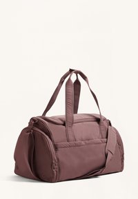 Duffel bag in muted mauve, made of soft, durable material. Features double handles and an adjustable shoulder strap, with multiple zippered pockets.