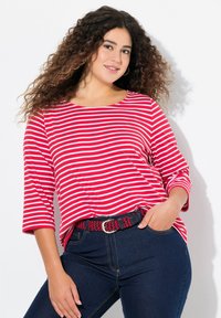 Rot-weiß gestreifte, locker sitzende Bluse mit Dreiviertelärmeln, kombiniert mit dunkelblauen Jeans und einem gemusterten Gürtel.
