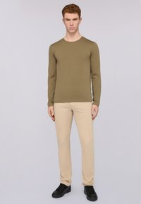 Olive green long-sleeve shirt with a round neckline paired with beige pants and black sneakers. Smooth texture, fitted design, minimal logo detail.